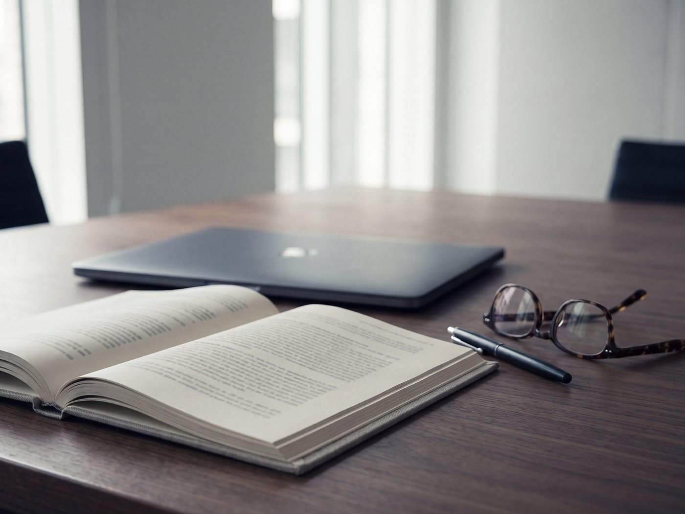 A closed laptop beside a printed report on a meeting table, reading glasses and a pen alongside